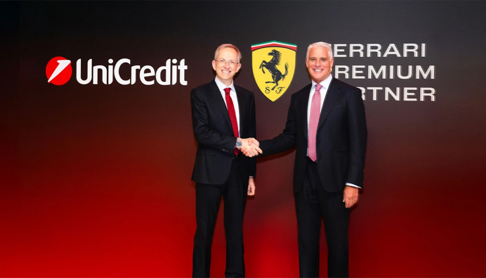 Dva muškarca u odijelima se rukuju ispred logotipa UniCredit / Ferrari